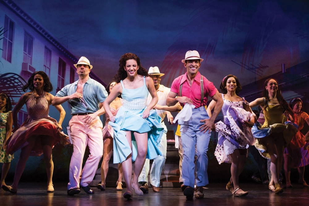 Actors on stage dance in colorful dresses and shirts